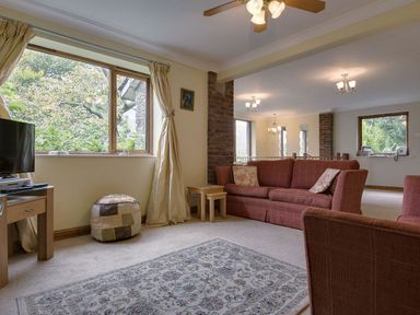A living room with red sofas a patterned rug a wooden table and large windows at Galanda Treetops in Newton Ferrers