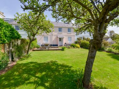 A garden with a lawn trees and a picnic table in front of a two story house at 4 Coastguards Cottage in Hope Cove
