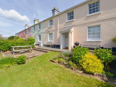 A row of pastel-colored terraced houses with outdoor benches a barbecue grill a picnic table and a garden at 4 Coastguards Cottage in Hope Cove