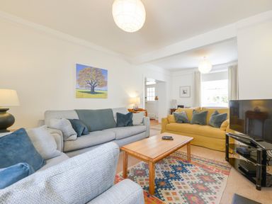 A living room with sofas cushions a wooden coffee table a patterned rug a television and a painting of a tree on the wall at 4 Coastguards Cottage in Hope Cove