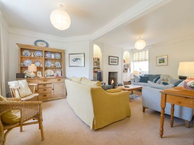 A living room with sofas a wooden cabinet with plates a fireplace and chairs at 4 Coastguards Cottage in Hope Cove