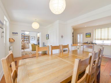 A dining area with a wooden table and chairs next to a kitchen and a living room at 4 Coastguards Cottage in Hope Cove
