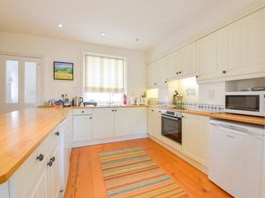 A kitchen with white cabinets wooden countertops a striped rug and appliances at 4 Coastguards Cottage in Hope Cove