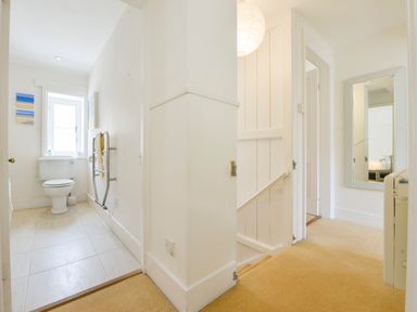 A hallway with carpeted floor a bathroom with toilet and towel rail and a staircase at 4 Coastguards Cottage in Hope Cove