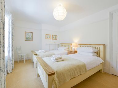 A bedroom with two single beds a bedside table with a lamp a chair and framed pictures on the wall at 4 Coastguards Cottage in Hope Cove