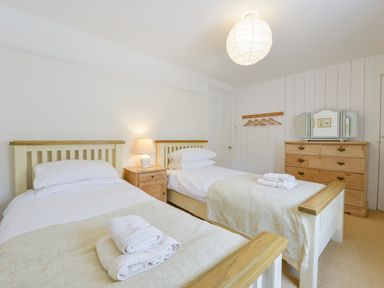 A bedroom with two single beds a nightstand with a lamp a wooden dresser and a wall rack at 4 Coastguards Cottage in Hope Cove