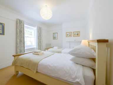 A bedroom with two single beds a window curtains and wall pictures at 4 Coastguards Cottage in Hope Cove