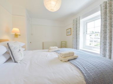 A bedroom with a bed folded towels a pillow a window with floral curtains and a wall lamp at 4 Coastguards Cottage Hope Cove