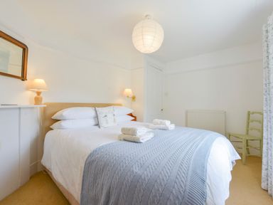 A bedroom with a double bed with folded towels bedside lamps a chair and a radiato at 4 Coastguards Cottage in Hope Cove