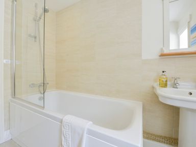 A bathroom with a bathtub a shower head a towel on the tub and a sink with soap at 4 Coastguards Cottage in Hope Cove