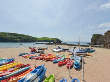 A sandy beach with rows of kayaks and boats near the water at 4 Coastguards Cottage in Hope Cove