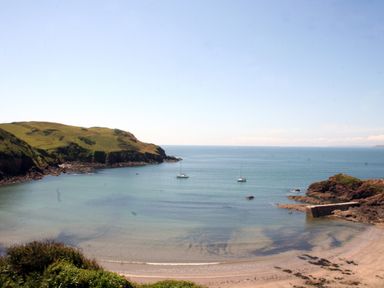 A beach with two boats in a bay surrounded by grassy cliffs at 4 Coastguards Cottage in Hope Cove