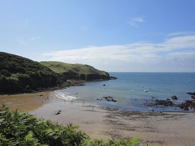 A beach with people on the sand and in the water boats on the water grassy hills in the background at 4 Coastguards Cottage Hope Cove