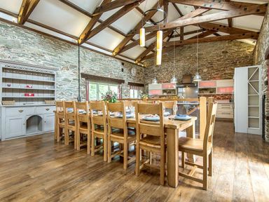 A large dining table with wooden chairs set for a meal in a kitchen with stone walls and exposed wooden beams at Mill Barn in Woolston near Salcombe