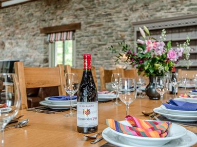 A dining table with wine bottles glasses plates with colorful napkins and a flower arrangement at Mill Barn in Woolston near Salcombe