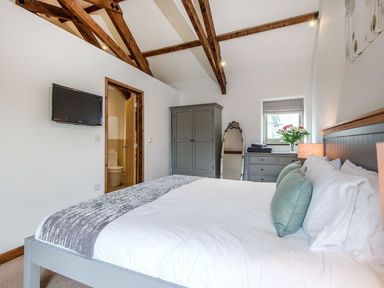 A bedroom with a bed pillows a wardrobe a dresser a mirror and a wall-mounted television at Mill Barn in Woolston near Salcombe