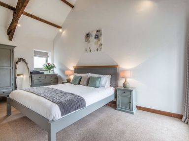 A bedroom with a grey bed and wooden beams on the ceiling at Mill Barn in Woolston near Salcombe