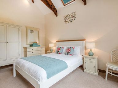 A bedroom with a double bed, bedside tables with lamps, a wardrobe, a dresser with a mirror, and a chair at Mill Barn in Woolston near Salcombe