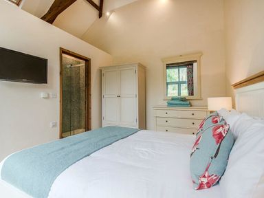A bedroom with a bed with pillows and a blanket a dresser with a mirror and towels a wardrobe a wall-mounted television and a shower room at Mill Barn in Woolston near Salcombe