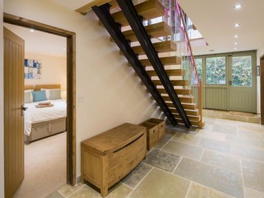 A hallway with stone tile floor wooden staircase wooden chest and green double doors at Mill Barn in Woolston near Salcombe