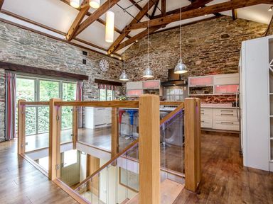 A kitchen with stone walls wooden beams and a staircase with glass and wood railing at Mill Barn in Woolston near Salcombe