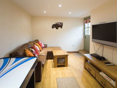 A living room with a brown leather sofa and colorful cushions a wooden coffee table a flat screen tv on a wooden tv stand and an air hockey table at Mill Barn in Woolston near Salcombe