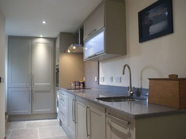 A kitchen with grey cabinets a sink a stove and a wooden box on the counter at Mill Barn in Woolston near Salcombe