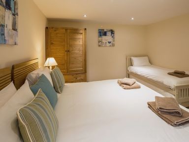 A bedroom with a double bed a single bed wooden wardrobe and bedside lamp at Mill Barn in Woolston near Salcombe