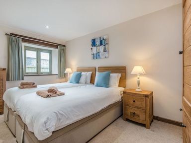 A bedroom with two single beds joined together bedside tables with lamps and a window with curtains at Mill Barn Woolston near Salcombe