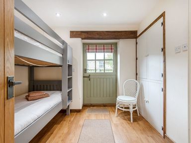 A small bedroom with a bunk bed towels on the lower bed white chair green door and built in cupboards at Mill Barn in Woolston near Salcombe