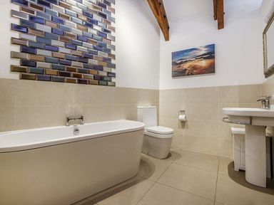 A bathroom with a bathtub toilet sink wall art and exposed wooden beams at Mill Barn Woolston near Salcombe