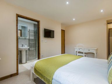 A bedroom with a bed green throw white desk attached bathroom and wall mounted television at Mill Barn in Woolston near Salcombe