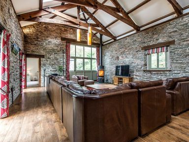 A living room with a large brown leather sofa a wood burning stove and a television on a wooden stand at Mill Barn in Woolston near Salcombe
