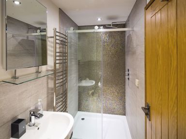 A bathroom with a sink mirror glass shower enclosure and a wooden door at Mill Barn in Woolston near Salcombe
