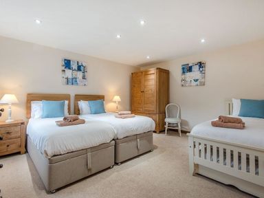 A bedroom with three beds two bedside tables lamps a wooden wardrobe and a chair at Mill Barn in Woolston near Salcombe
