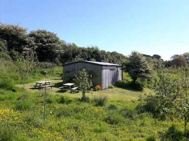 A garden shed with two picnic tables and a swing set in a grassy area with trees at Mill Barn in Woolston near Salcombe