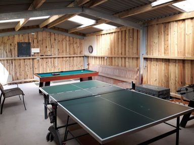 A game room with a ping pong table pool table wooden bench and dart board at Mill Barn in Woolston near Salcombe