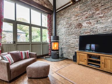 A living room with a wood burning stove a sofa and a television at Mill Barn in Woolston near Salcombe