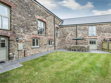 A grassy yard with stone walls and an outdoor dining table with chairs and an umbrella at Mill Barn in Woolston near Salcombe