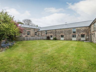 A grassy courtyard surrounded by stone buildings with multiple windows and doors at Mill Barn in Woolston near Salcombe