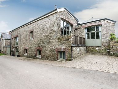 An exterior view of a stone building with multiple windows and a paved driveway at Mill Barn in Woolston near Salcombe