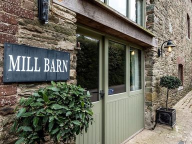 The entrance of a stone building with green double doors and a sign that reads Mill Barn Woolston near Salcombe