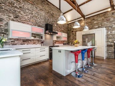 A kitchen with stone walls a large island with colorful stools and hanging lights at Mill Barn in Woolston near Salcombe