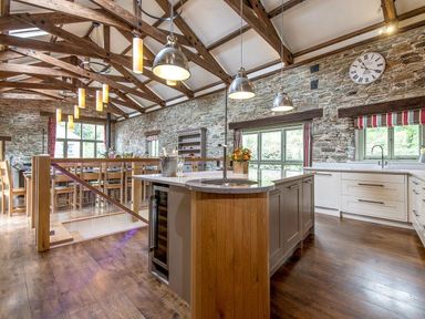 A kitchen and dining area with wooden beams stone walls and large windows at Mill Barn in Woolston near Salcombe