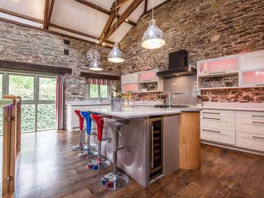 A kitchen with stone walls an island with stools and a wooden floor at Mill Barn Woolston near Salcombe