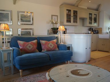 A living room with a sofa and kitchen area at Coach House Cottage, Strete, near Dartmouth