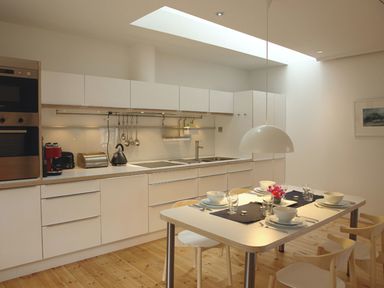 A kitchen with white cabinets a dining table set for four and wooden chairs at The Gallery in Aveton Gifford