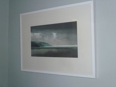 A framed landscape painting on a gray wall at The Gallery in Aveton Gifford