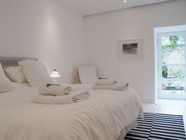 A bedroom with a bed with white linens and towels and a chair next to a window at The Gallery in Aveton Gifford