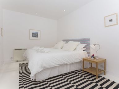 A bedroom with a double bed pillows and folded towels on a striped rug with a wooden bedside table and lamp at The Gallery in Aveton Gifford